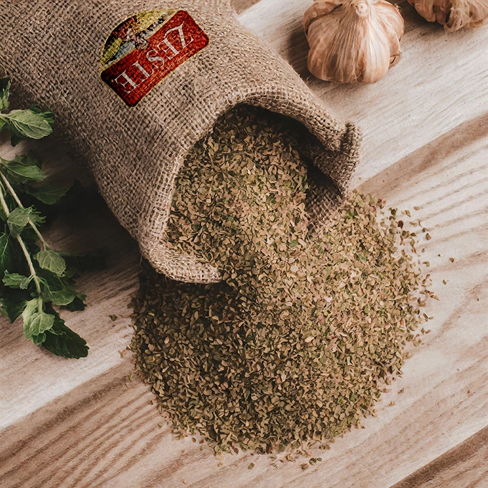 Organic oregano spilling from a burlap sack on a wooden surface, surrounded by fresh oregano leaves and garlic bulbs.